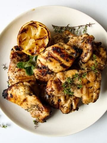 Grilled Boneless Chicken Thighs piled on a white plate garnished with thyme.