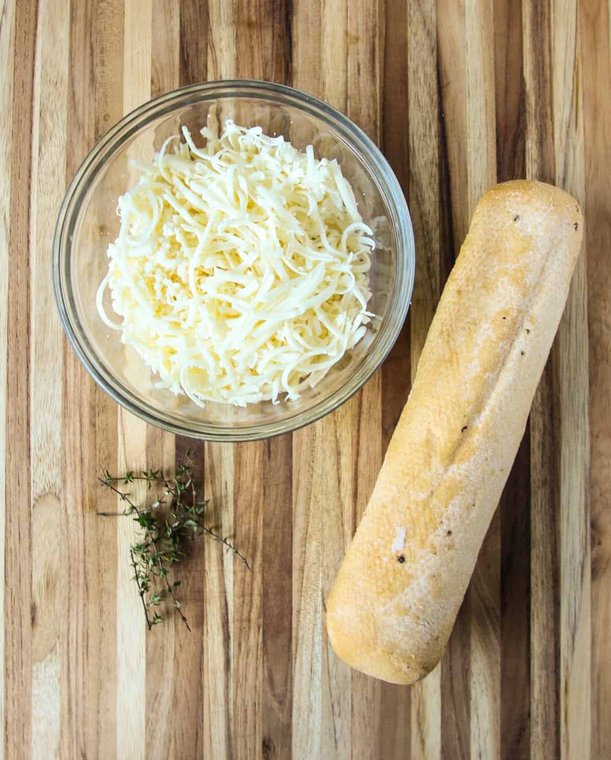 A baguette and a bowl of shredded cheese to be used in the soup recipe.