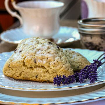 A lavender scone on a China plate with a teacup in the background.