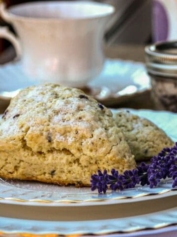 A lavender scone on a China plate with a teacup in the background.