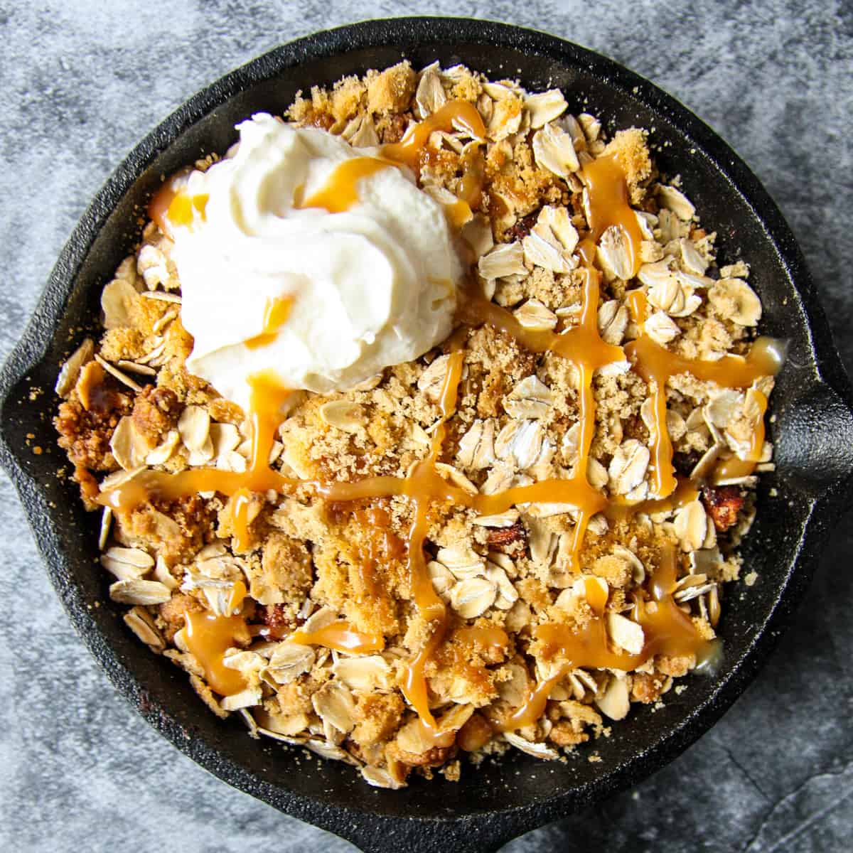 Air fryer apple crisp in a cast iron pan, topped with a dollop of whipped cream.