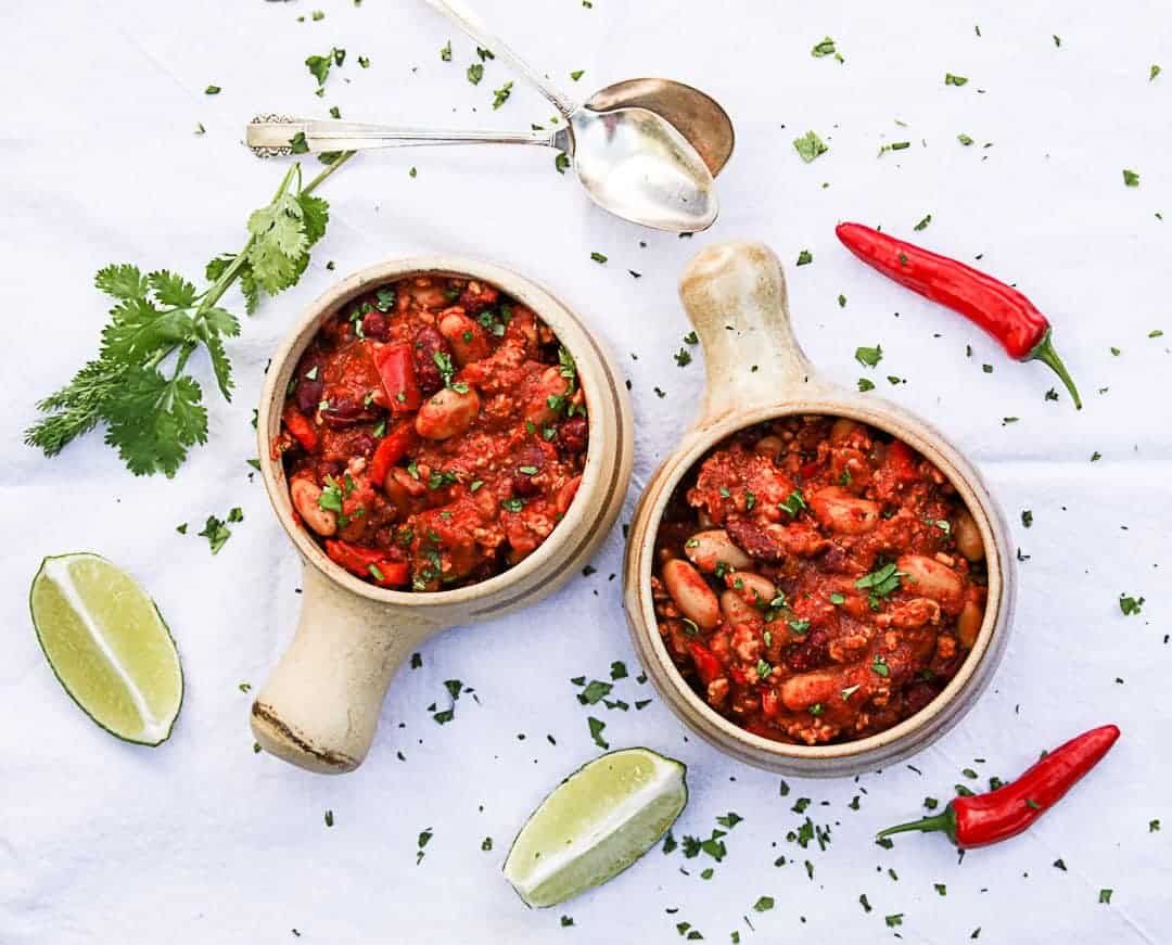 Two bowls of food on a table, with spoons and lime wedges