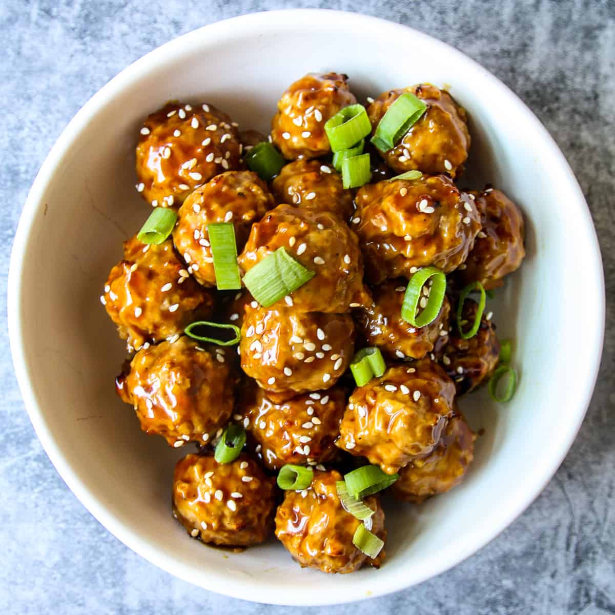 Asian chicken meatballs in a white bowl, garnished with green onion slices.