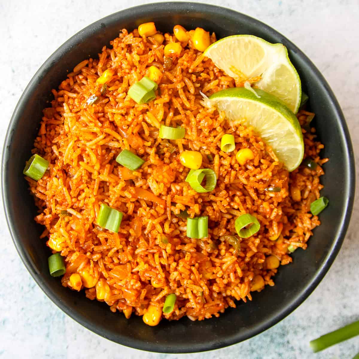 Mexican fried rice in a black bowl, garnished with lime wedges.