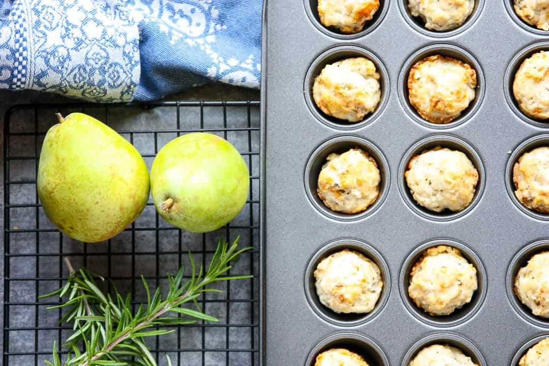 Mini muffin pan of pear gorgonzola appetizer bites with two pears and a sprig of rosemary