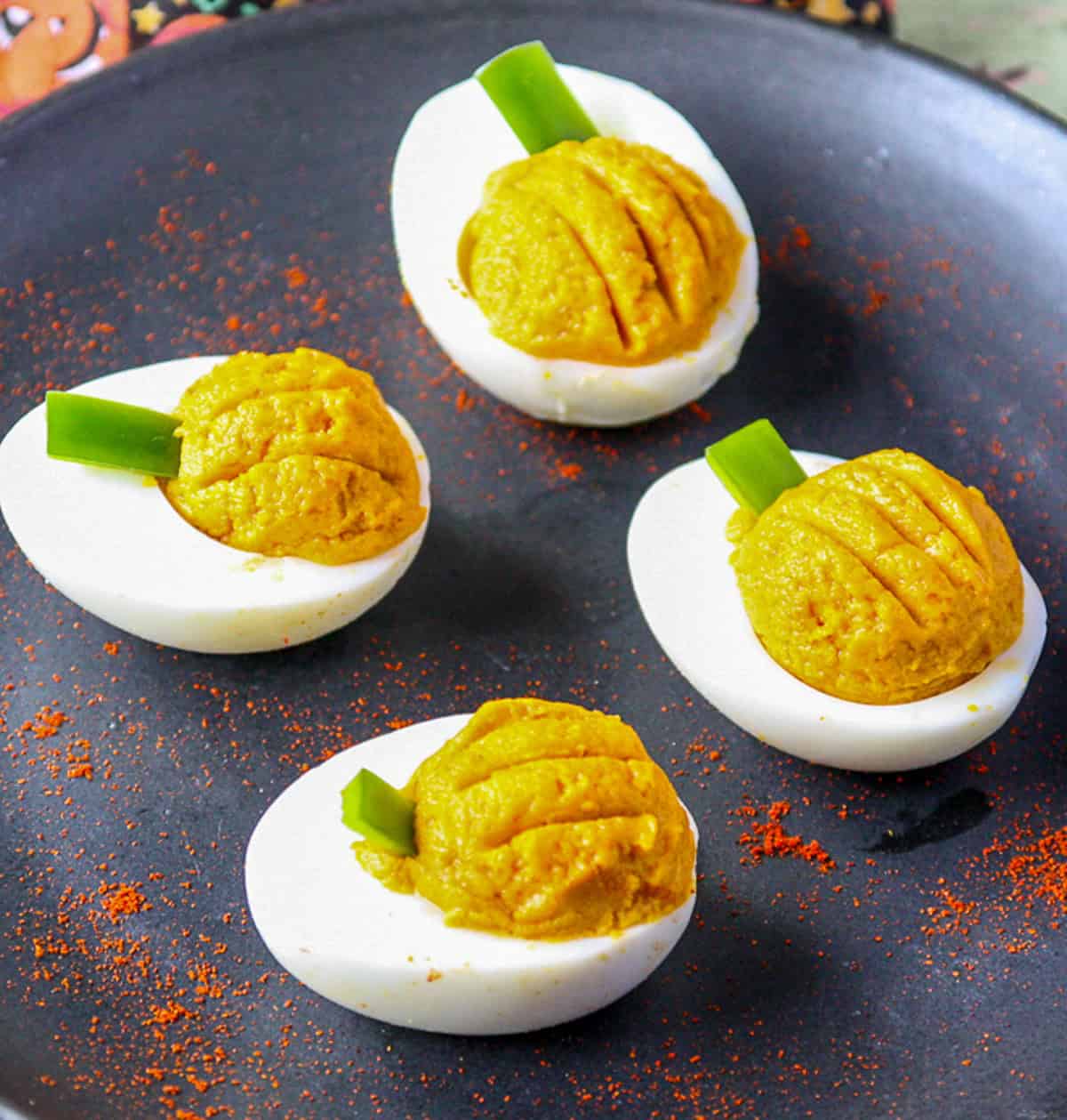 Deviled eggs styled as mini pumpkins on a black plate.
