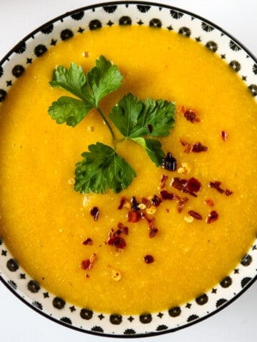 Overhead view of a bowl of carrot soup garnished with cilantro and chili flakes.