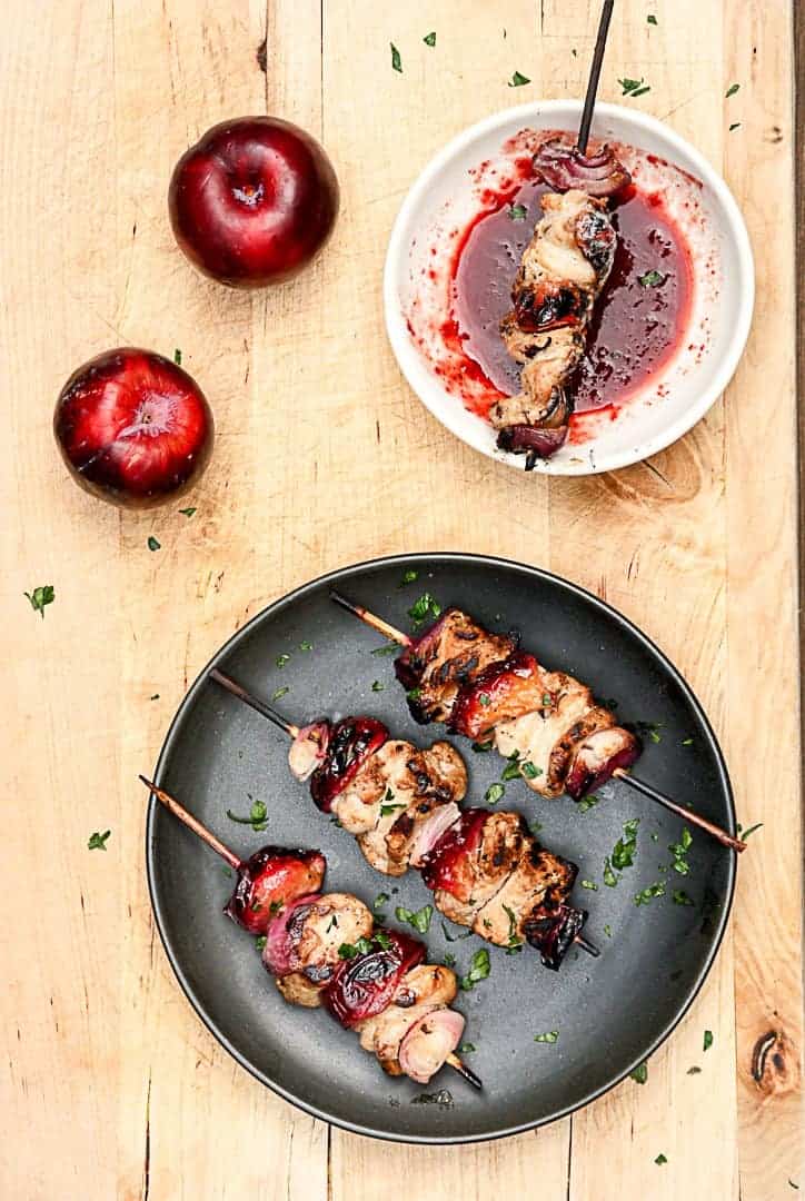 3 skewers of pork and plums on a black plate