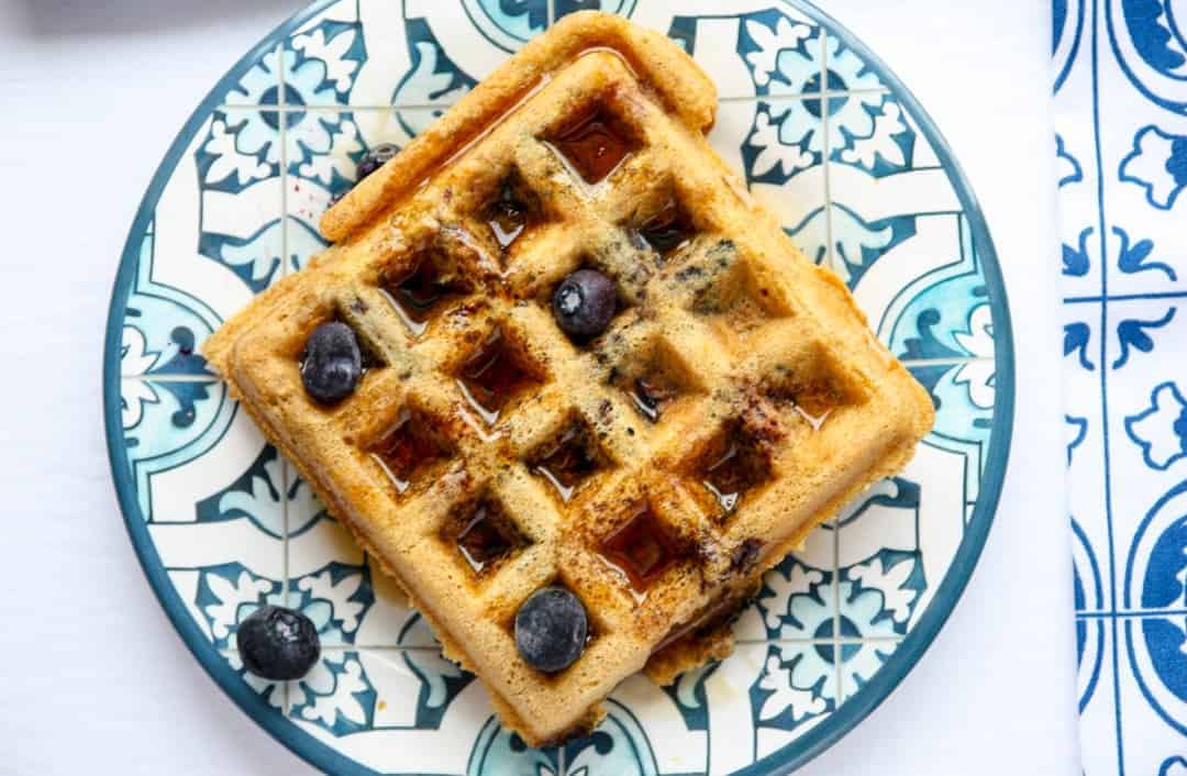 A waffle on a blue plate, with blueberries and syrup