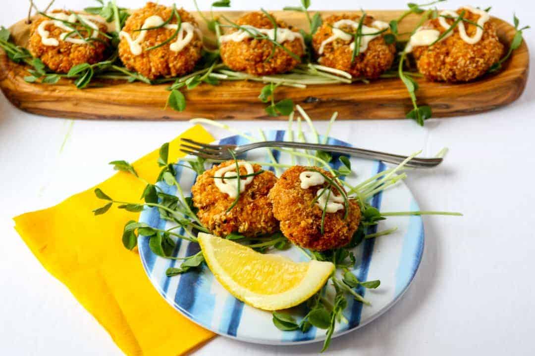 Crab cakes on a plate, with a tray of crab cakes