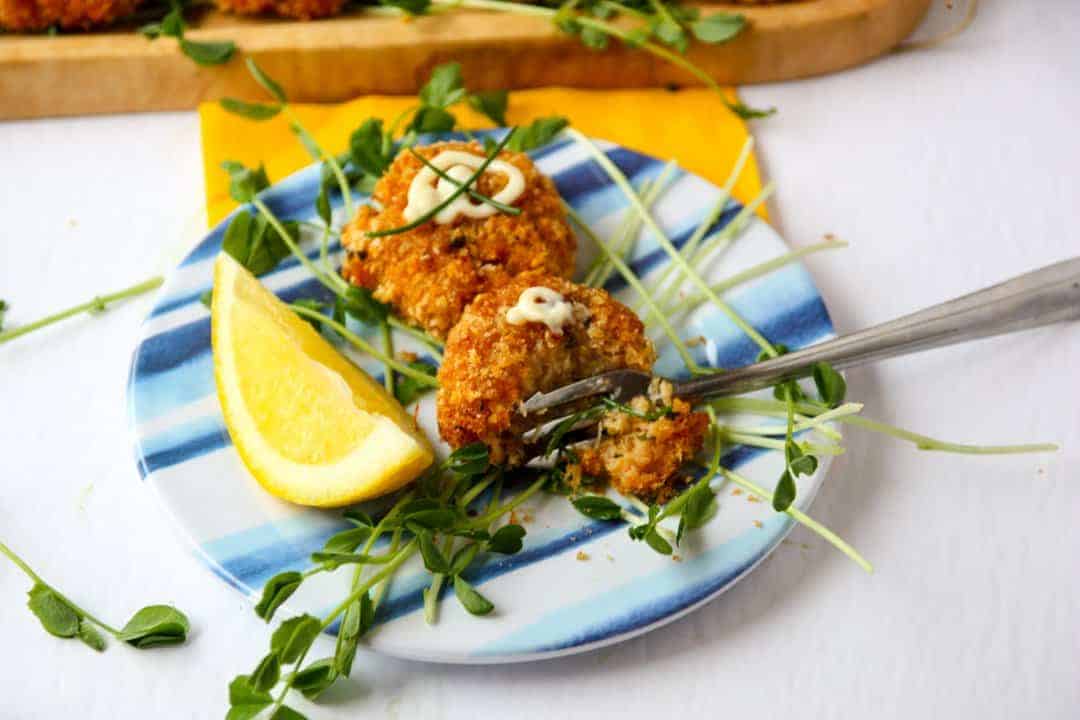 Two Cajun Crab Cakes on a small blue & white plate with peas shoots and a lemon wedge.