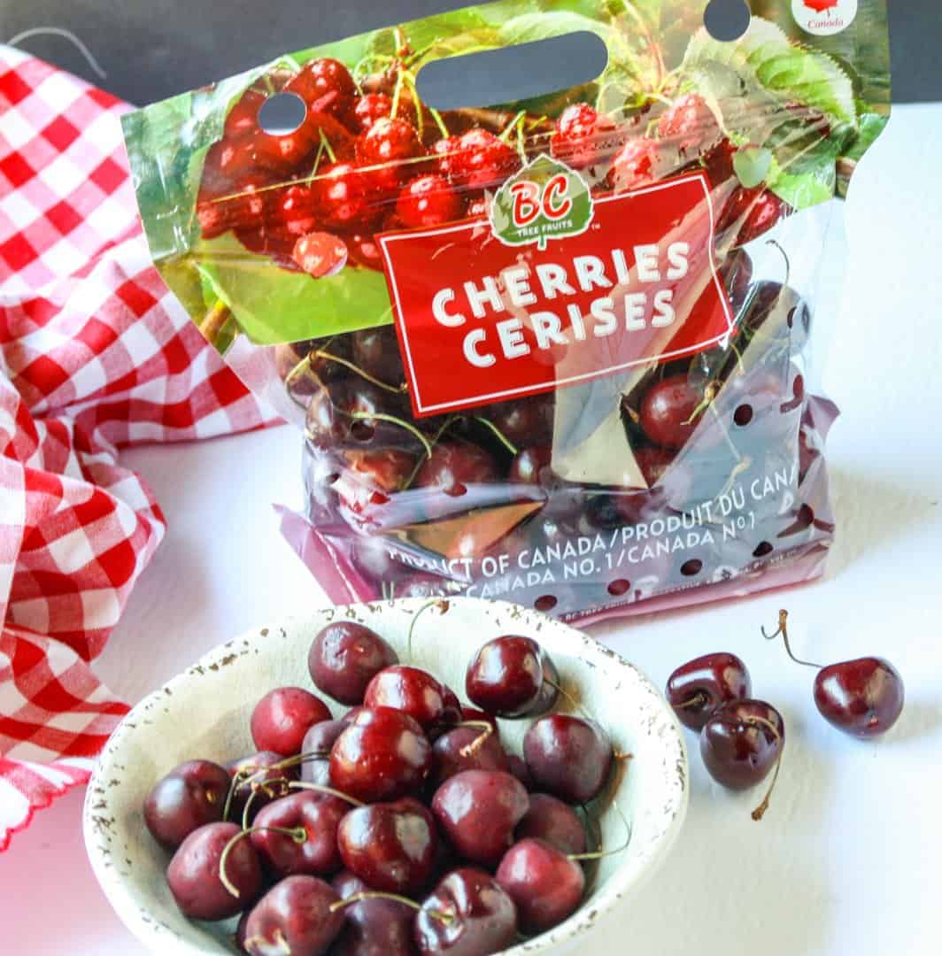 A package of cherries next to a bowl of cherries on a table