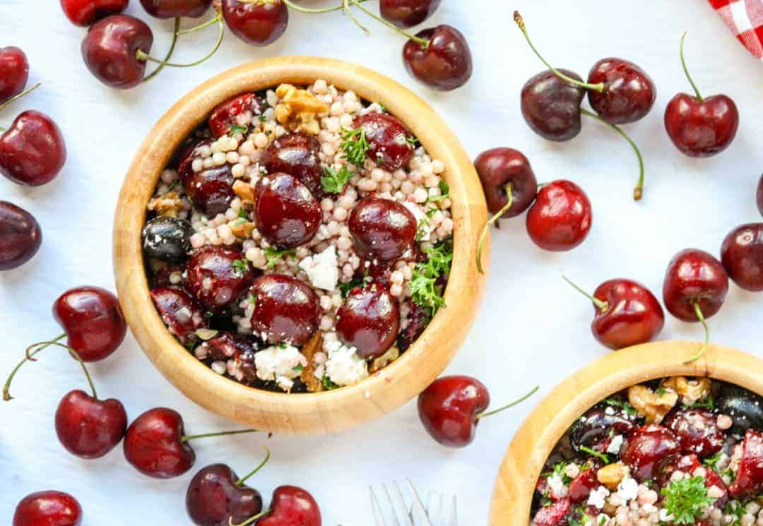 A bowl of salad sitting on top of a table, with Cherries