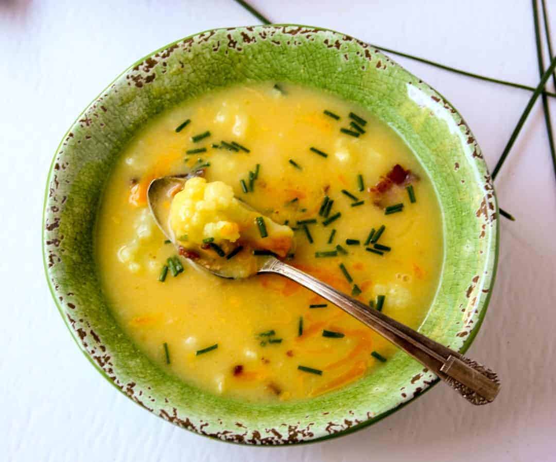 Green bowl cheesy cauliflower soup with silver spoon