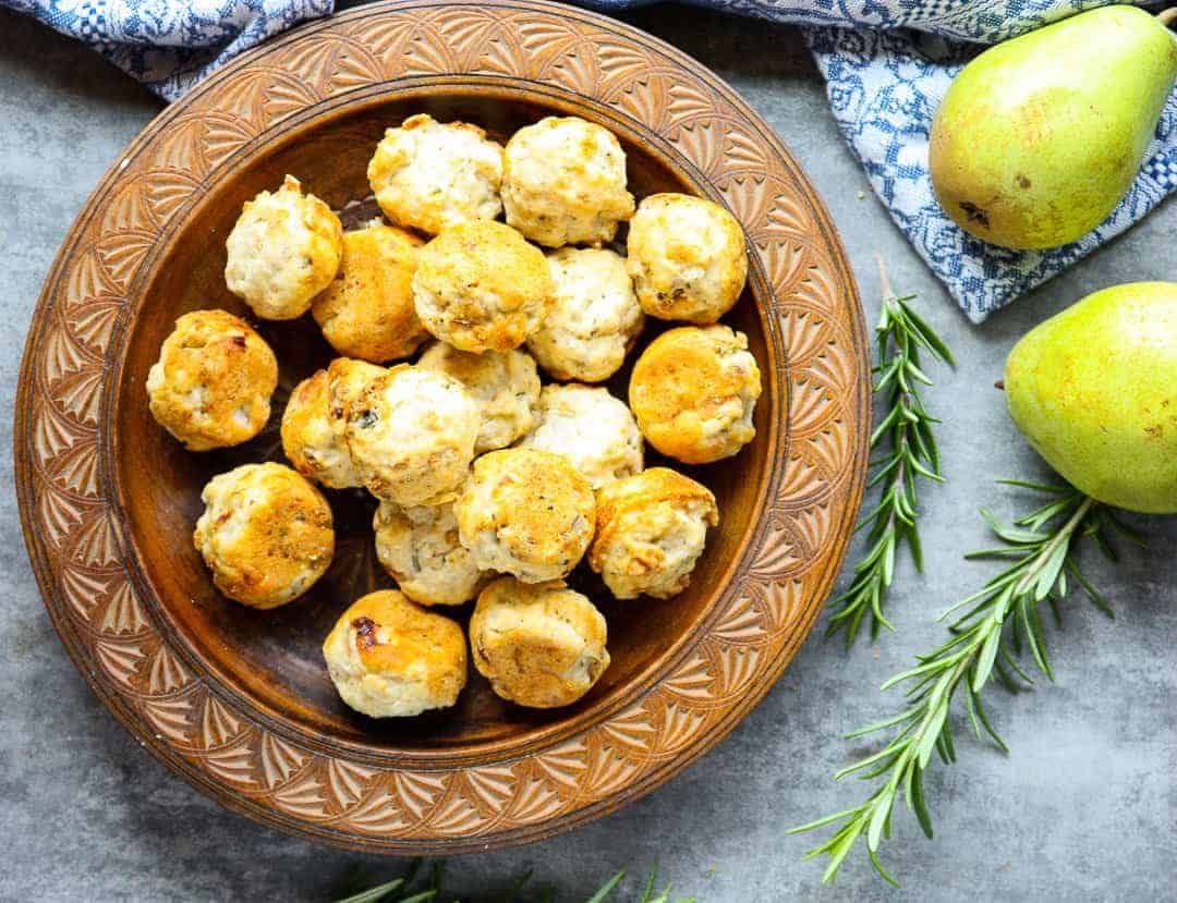 Wooden plate of pear & gorgonzola mini muffins beside two pears and sprigs of rosemary