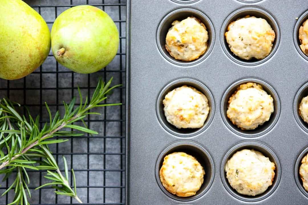 Mini muffins in a pan on a rack, with a pear