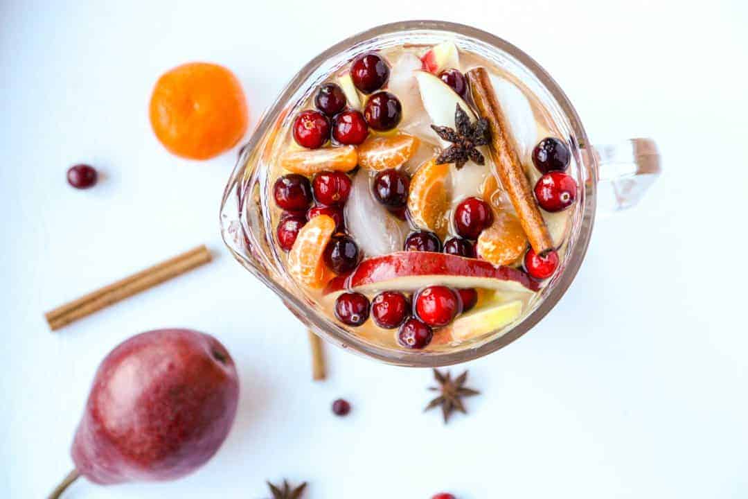 Top down view of carafe of sangria filled with cinnamon sticks, apple slices, orange slices, and cranberries