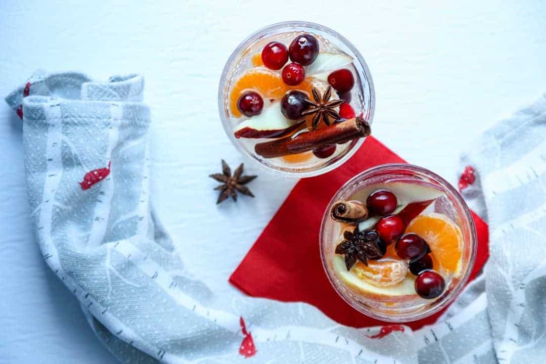 Two glasses of of sangria filled with cinnamon sticks, apple slices, orange slices, and cranberries