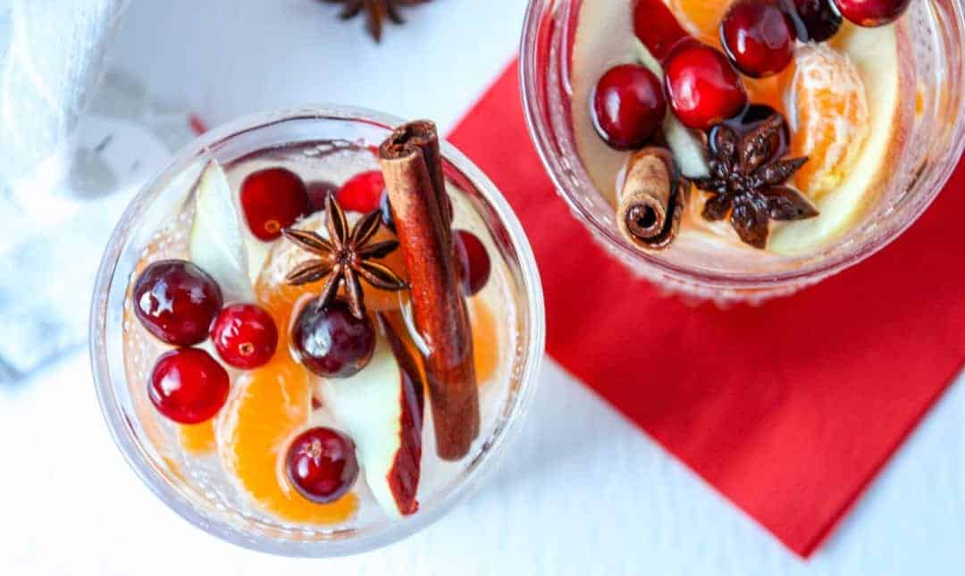 Top down view of two glasses of sangria filled with cinnamon sticks, apple slices, orange slices, and cranberries