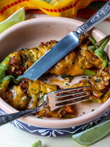 Two stuffed Anaheim peppers in a terra cotta dish.