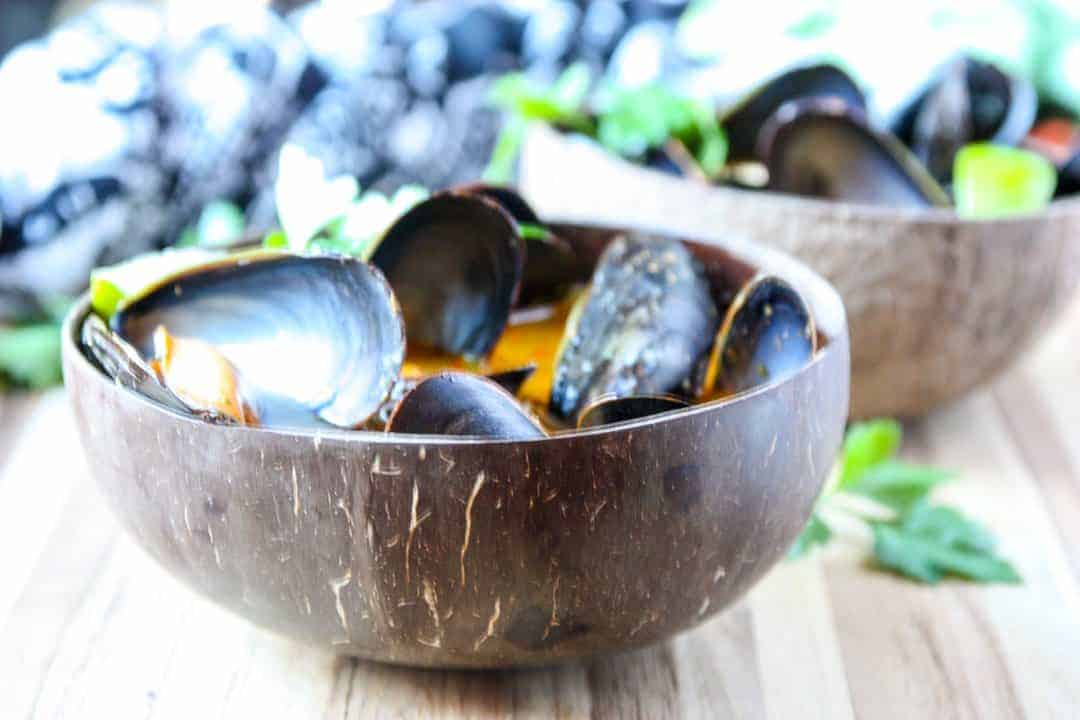 Mussels in orange broth in brown wooden bowl on wooden table