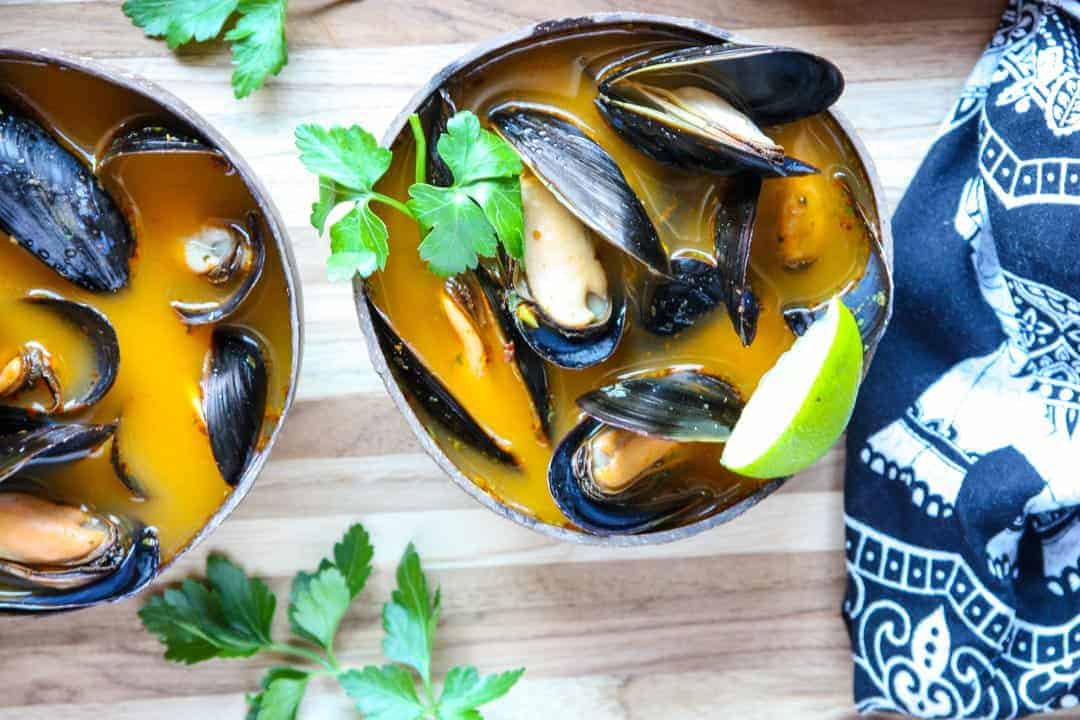 Mussels in orange broth in brown wooden bowl on wooden table