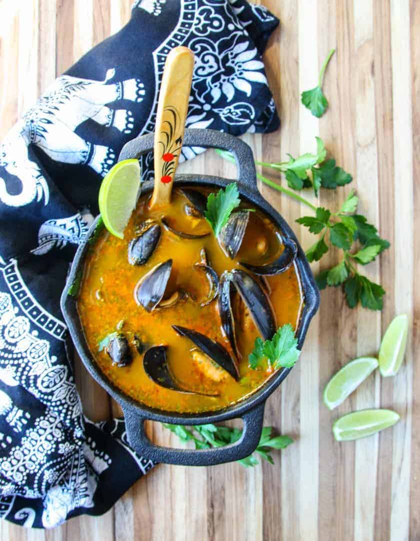 Mussels thai style in orange broth in brown wooden bowl on wooden table