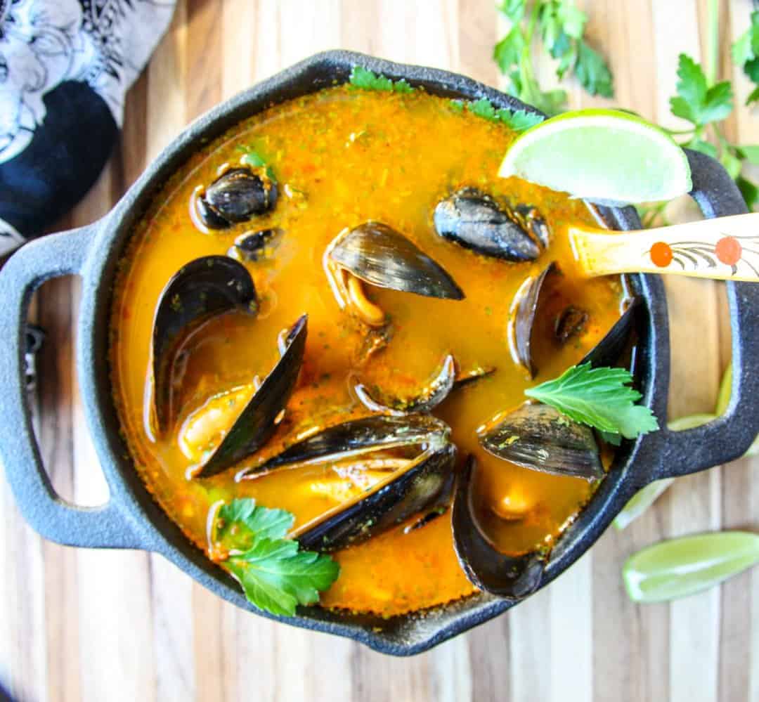 A pot of shellfish in orange broth on wooden table