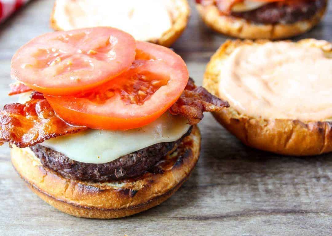 A burger topped with bacon, cheese and tomato