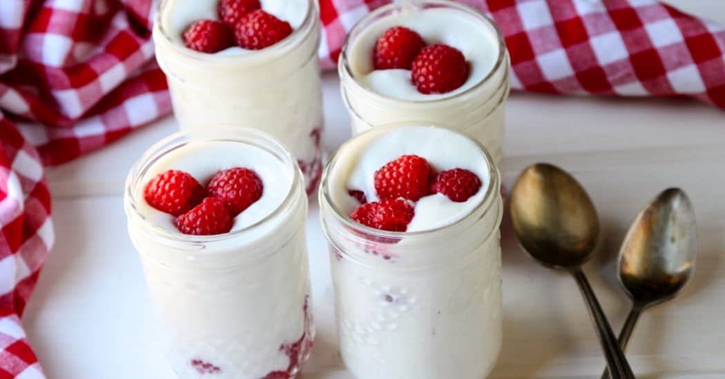 Jars of mousse topped with raspberries on top of a table
