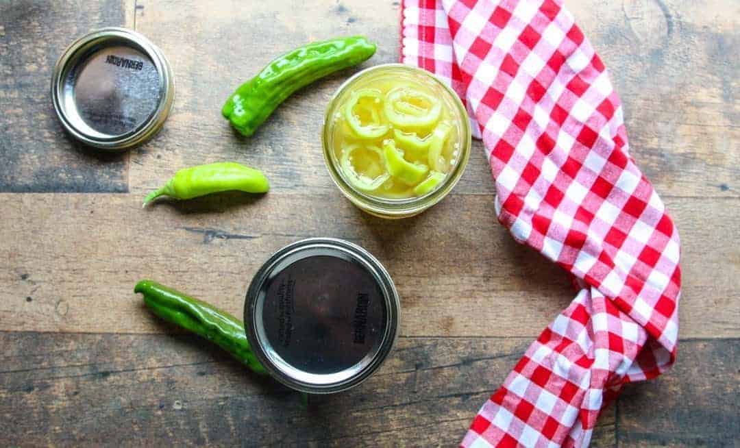 A close up of jars of pickles on a table, with peppers