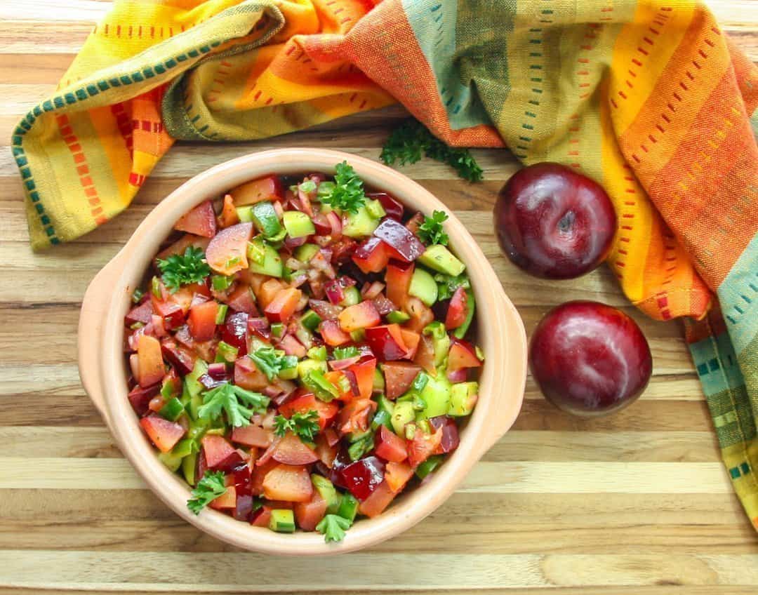 A bowl of fruit salsa on top of a wooden table, with Plums