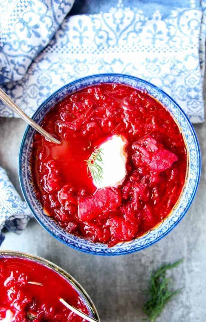 Blue and white bowl filled with red Ukrainian borscht with sour cream dollop on top