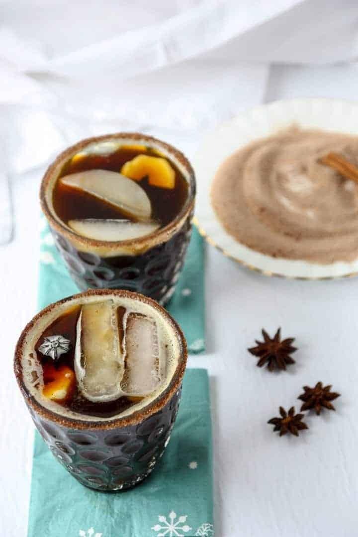 Two cocktails in glasses on blue napkins next to cinnamon sugar on a round white plate