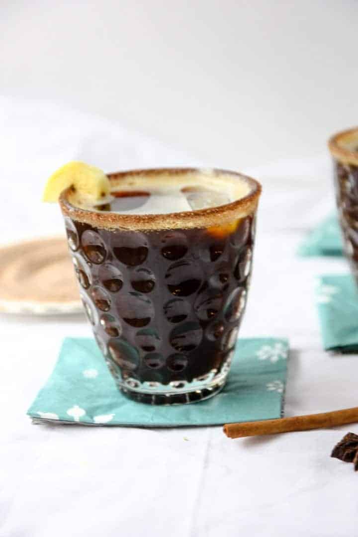 Cocktail in a glass on blue napkin next to cinnamon sugar on a round white plate