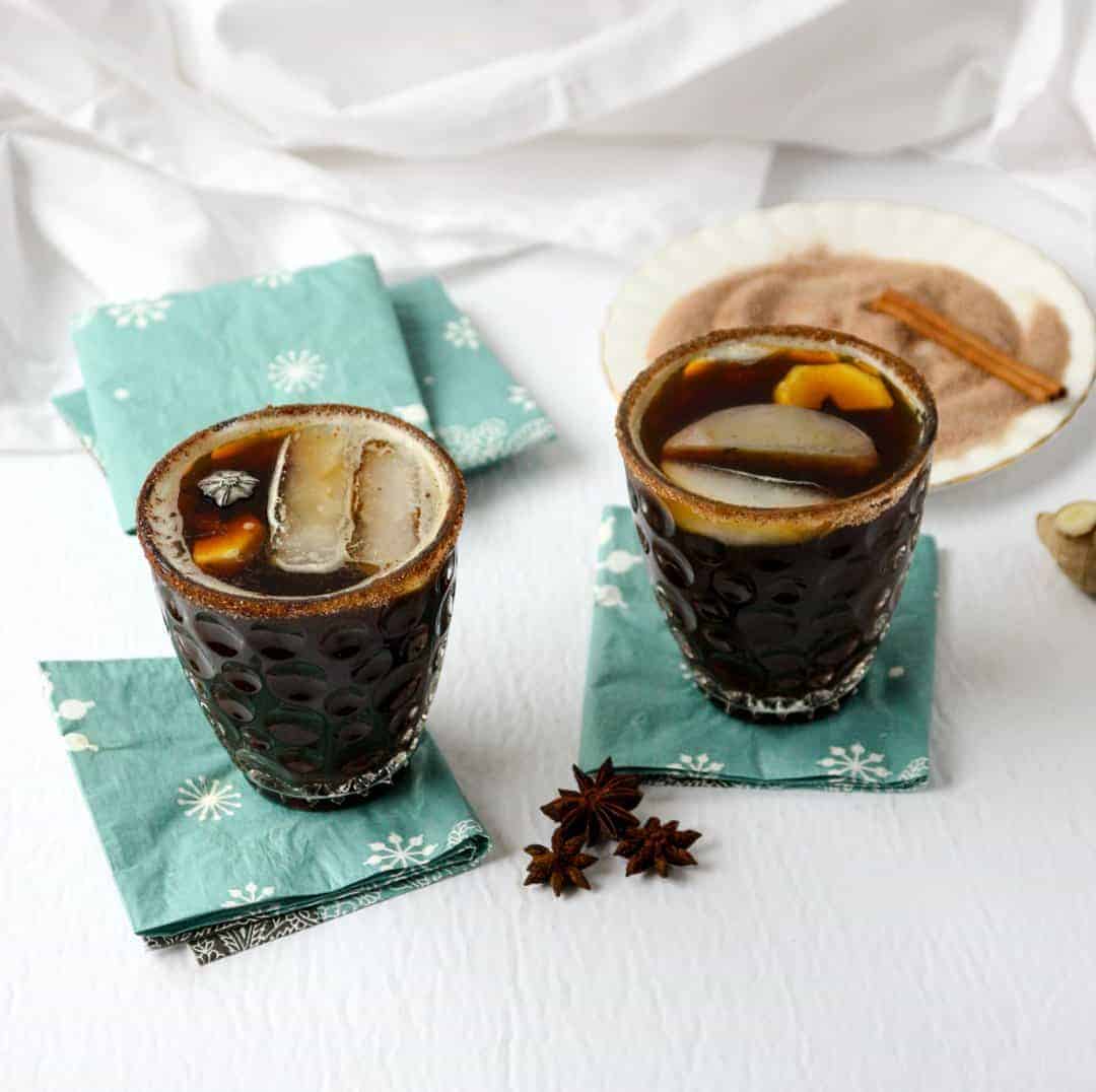 Two cocktails in glasses on blue napkins next to cinnamon sugar on a round white plate