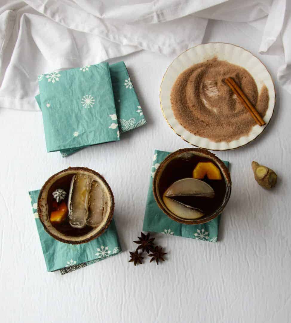 Two cocktails in glasses on blue napkins next to cinnamon sugar on a round white plate