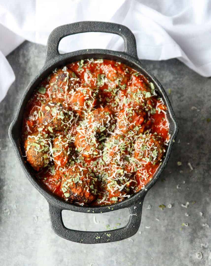 Top shot of meatless mushroom meatballs in marinara sauce, topped with parmesan cheese in black pot