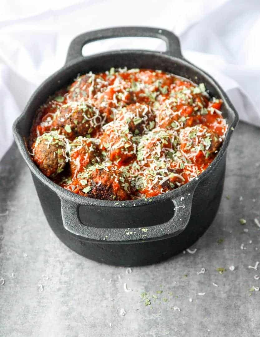 Top shot of meatballs in marinara sauce, topped with parmesan cheese in black pot