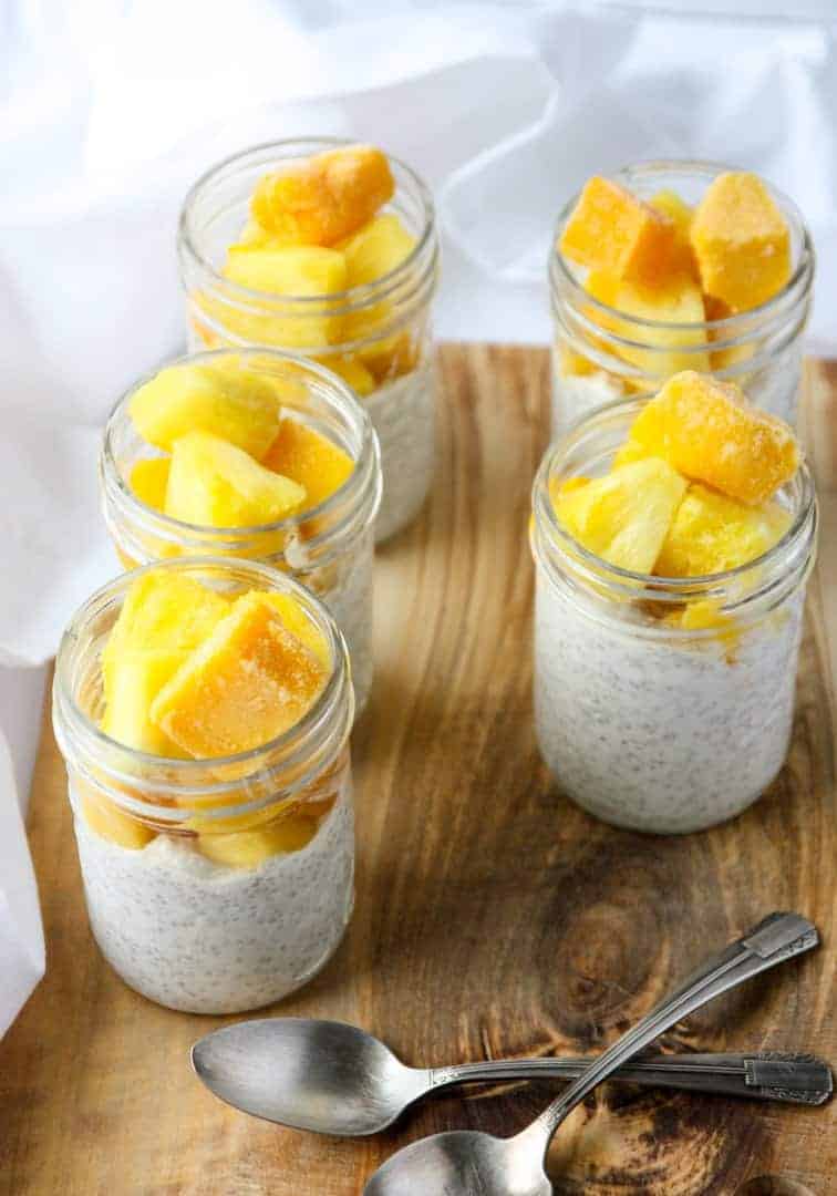 Four glass jars with coconut chia pudding and fruit.