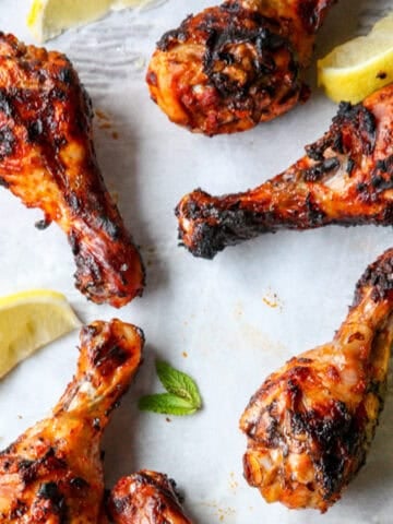 Four grilled harissa chicken drumstick with lemon wedges on a platter.