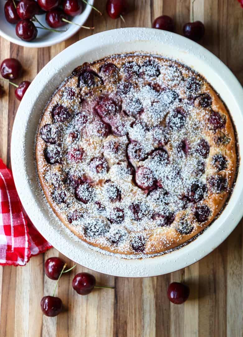 top shot of Cherry Almond Clafoutis on wooden table next to cherries