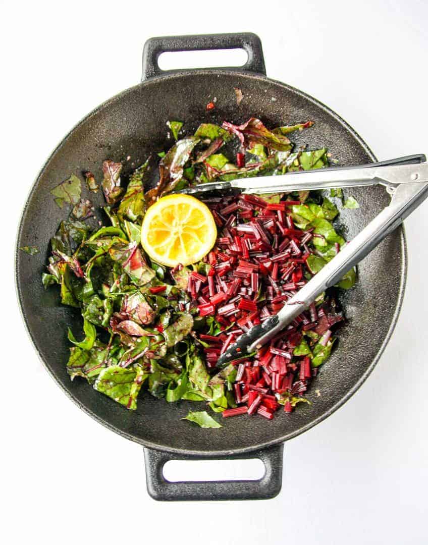 A pan of greens being sautéed with tongs.