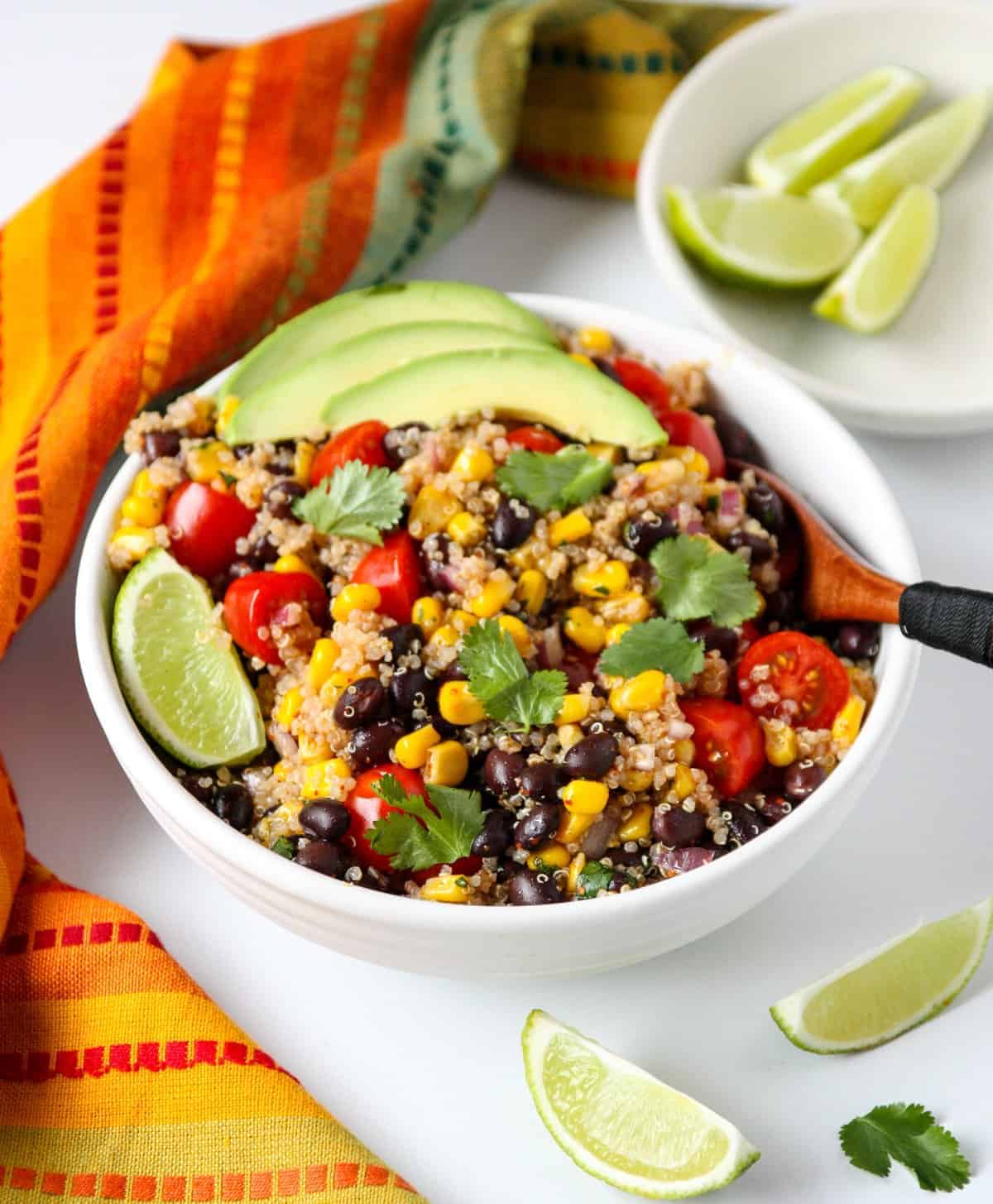 A bowl of Southwestern Quinoa Salad topped with avocado slices with a wooden fork.