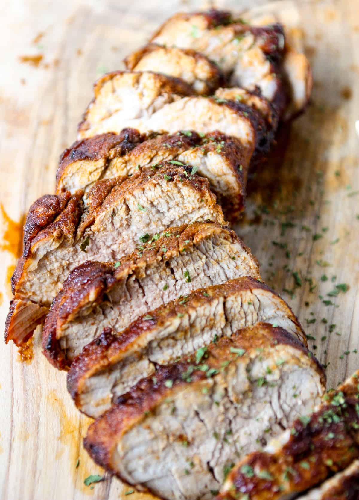 Slices of air fried pork tenderloin on a wooden cutting board.