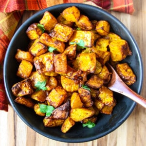 Air fryer butternut squash cubes in a bowl with a wooden spoon.