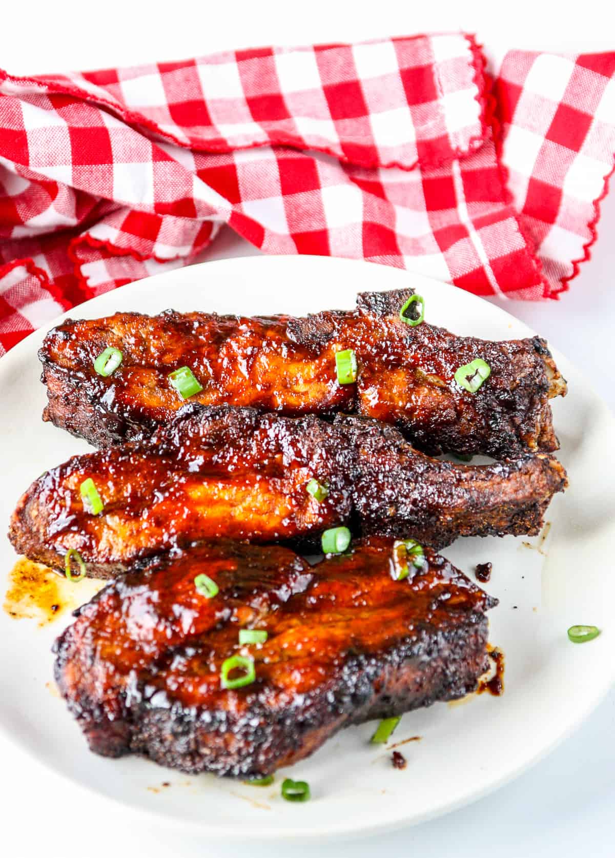 Three ribs covered in barbecue sauce on a white plate.