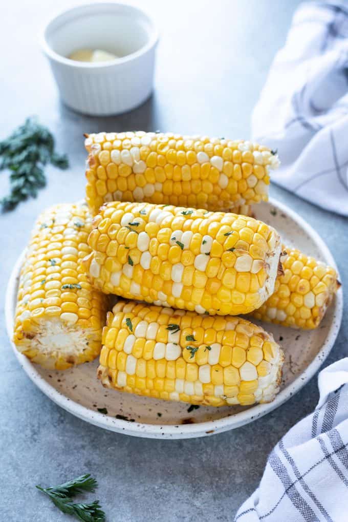 Five air fried corn on the cob garnished with parsley on a white plate.