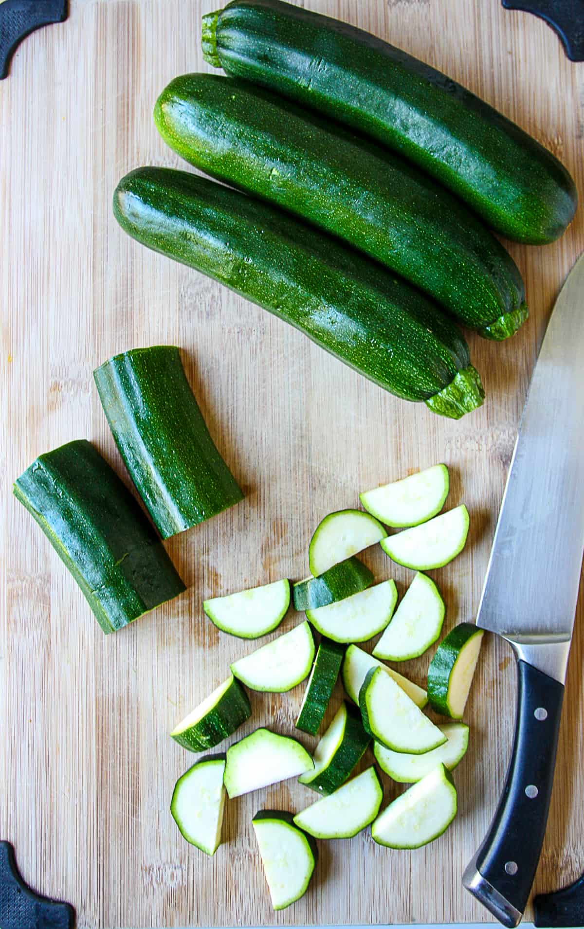 Zucchini being sliced on a cutting board.