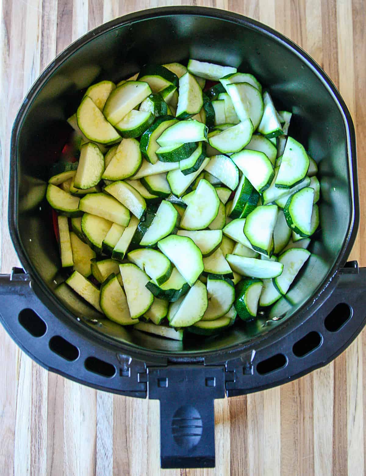 Zucchini slices being added to the basket of an air fryer.